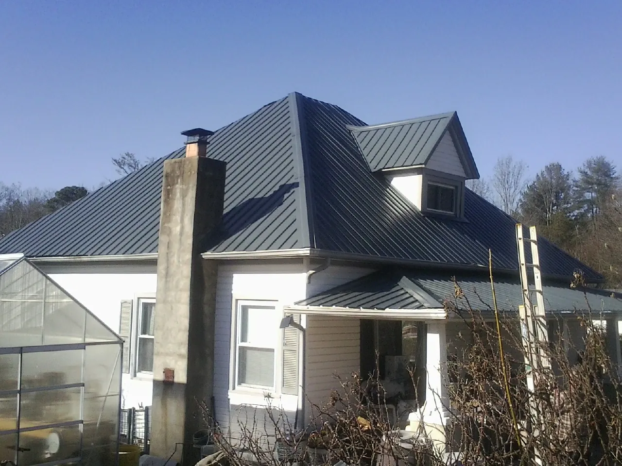 Dark blue standing seam metal roof on a white farmhouse with dormer — Slate & Tile Roof Repair by Roofing Brothers in Melba