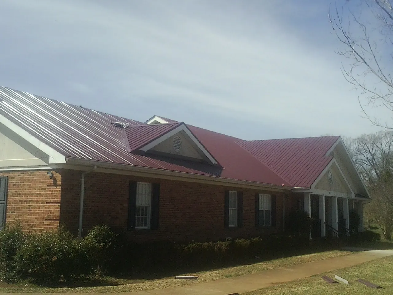 Red metal roof with gabled entries on a long brick building, from a Hail Damage Roof Repair job in Melba