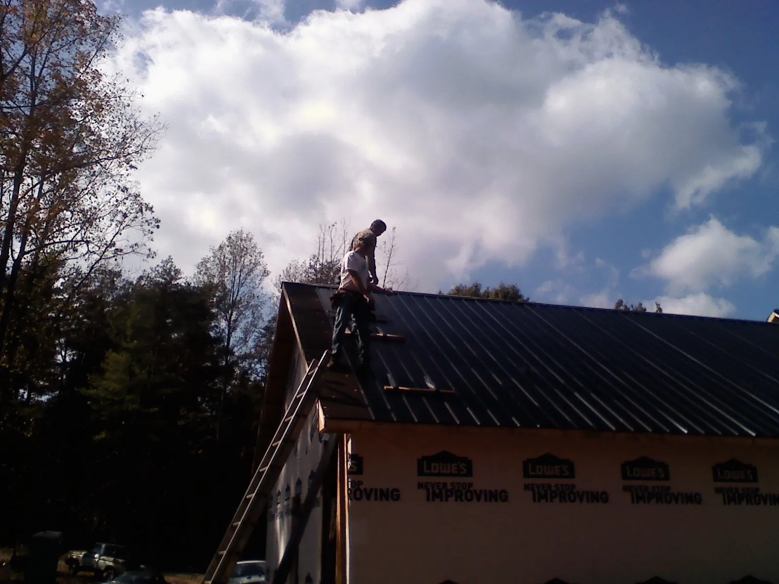Roofer fastening dark metal panels high against a cloudy sky, from a Roof Inspection job in Melba