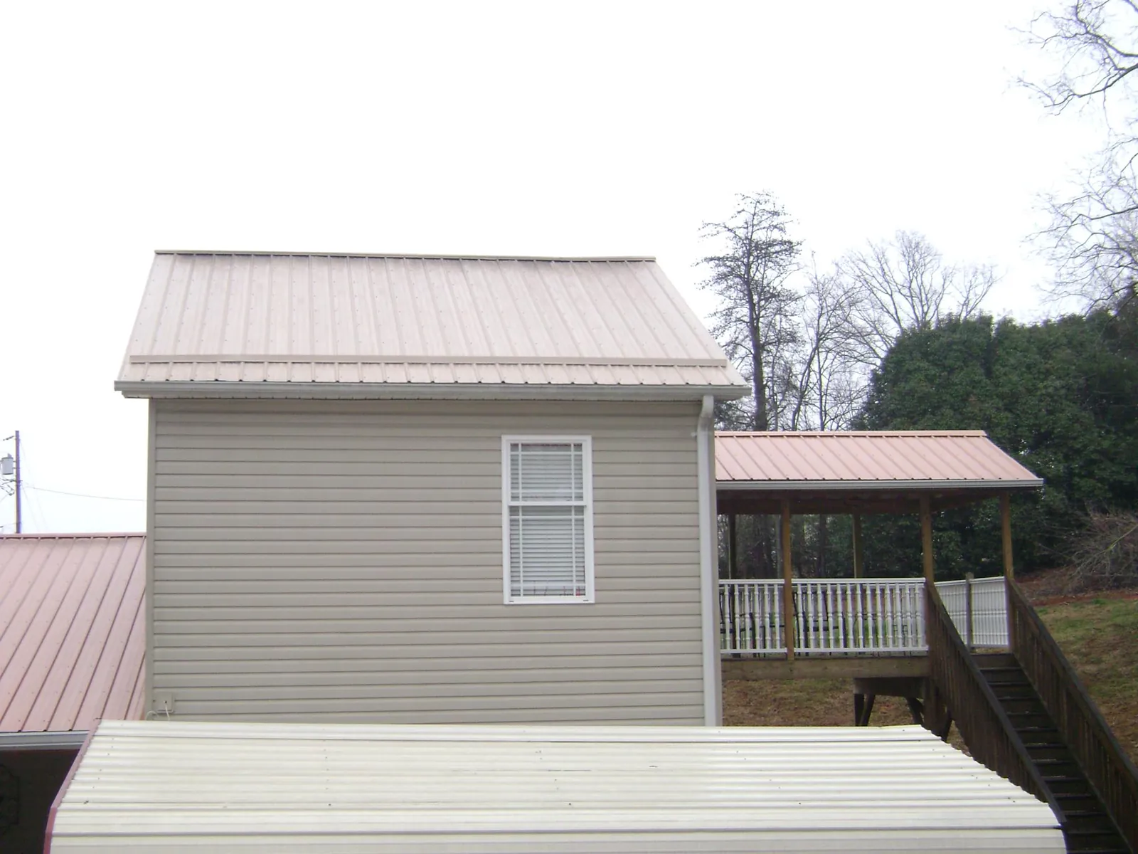 Tan metal roofs on a two story addition and attached porch, from a Roof Replacement job in Melba